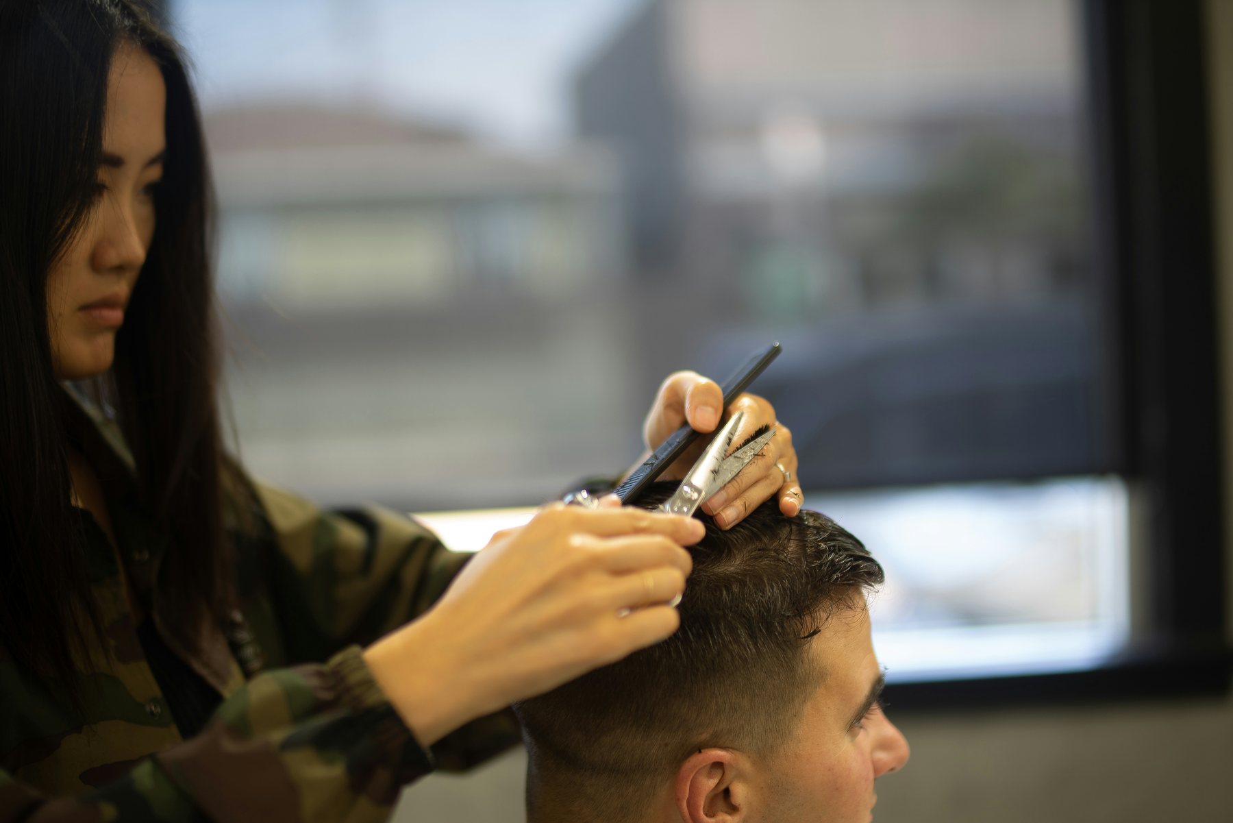 Stylist using scissor point cutting near a sunlit window to detail the top of a haircut